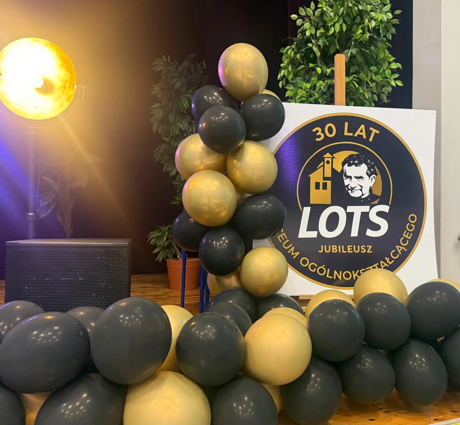 Balloon column in black and gold with a sign reading '30 LAT LOTS' and a yellow-stage light in the foreground.